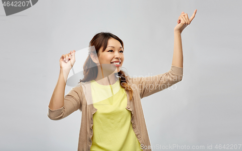 Image of happy asian woman dancing over grey background