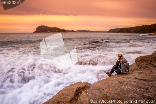 Image of Woman sits by the ocean watching the waves flow back and forth