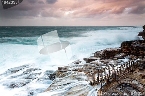 Image of Large swells engulf the rock shelf  at sunset