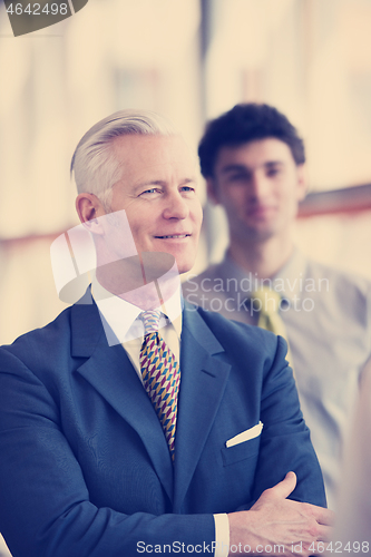 Image of portrait of senior businessman as leader  with staff in backgrou