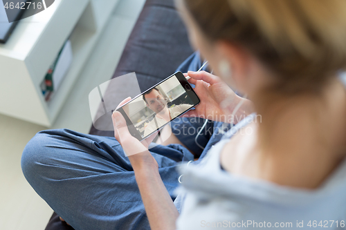 Image of Woman at home relaxing on sofa couch using social media on phone for video chatting with her loved ones during corona virus pandemic. Stay at home, social distancing lifestyle.