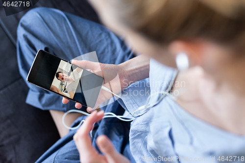 Image of Woman at home relaxing on sofa couch using social media on phone for video chatting with her loved ones during corona virus pandemic. Stay at home, social distancing lifestyle.