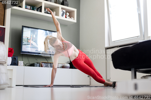 Image of Attractive sporty woman working out at home, doing pilates exercise in front of television in her living room. Social distancing. Stay healthy and stay at home during corona virus pandemic