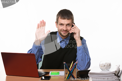 Image of The man sitting at the table and talking on the phone raised his hand in greeting