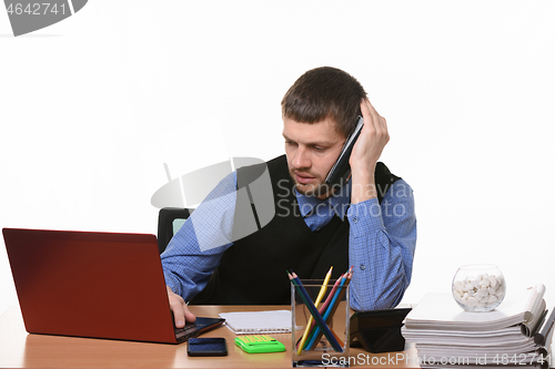 Image of A tired employee negotiates on the phone looking into the screen of the laptop