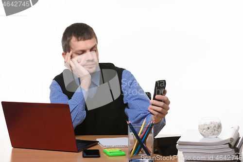 Image of Office worker dials number on phone sitting at desk