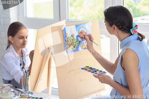 Image of Mom and daughter spend leisure time at home painting on easels by the window