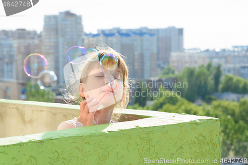 Image of A child is having fun on the balcony of a multi-storey building blowing soap bubbles
