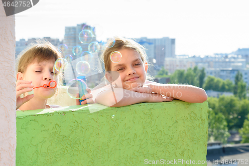 Image of Two girls blow bubbles on the balcony of a multi-storey building