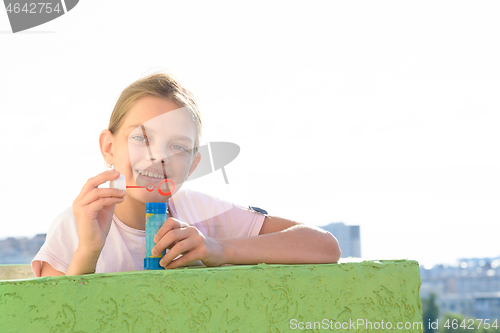 Image of Happy girl on the balcony of a high-rise building stands with a jar of soap bubbles