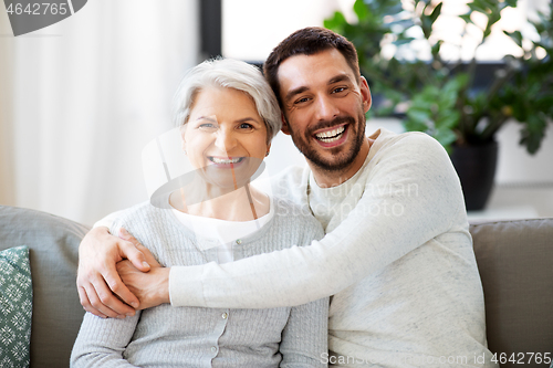 Image of senior mother with adult son hugging at home