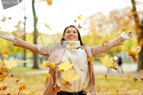 Image of happy woman having fun with leaves in autumn park