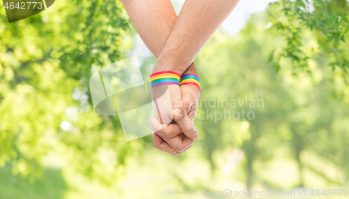 Image of hands of couple with gay pride rainbow wristbands