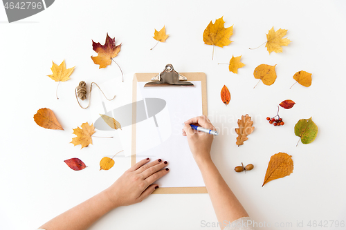 Image of hands writing on paper on clipboard in autumn