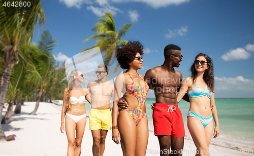 Image of happy friends walking along summer beach