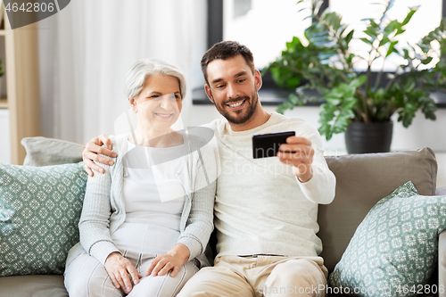 Image of senior mother with adult son taking selfie at home