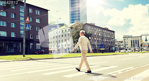 Image of senior man walking along city crosswalk