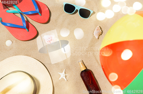 Image of hat, flip flops and shades and beach ball on sand