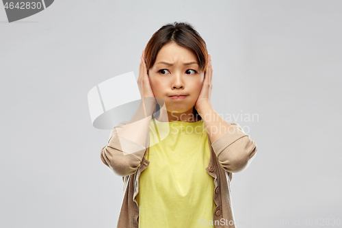 Image of asian woman closing ears by hands