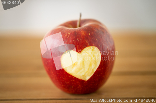 Image of red apple with carved heart shape on wooden table