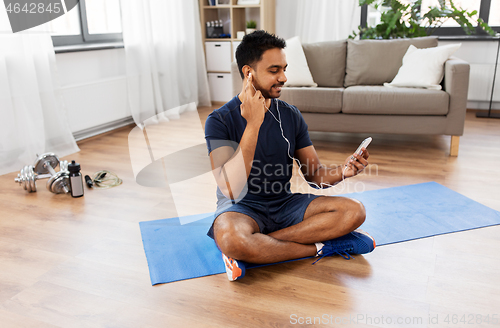 Image of indian man with smartphone on exercise mat at home