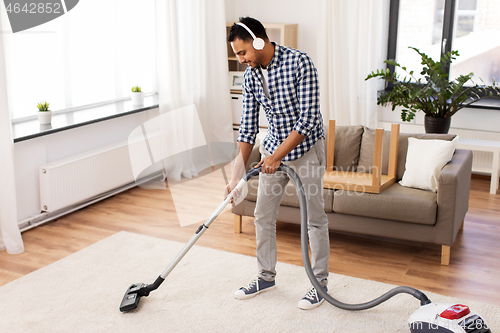 Image of man in headphones with vacuum cleaner at home