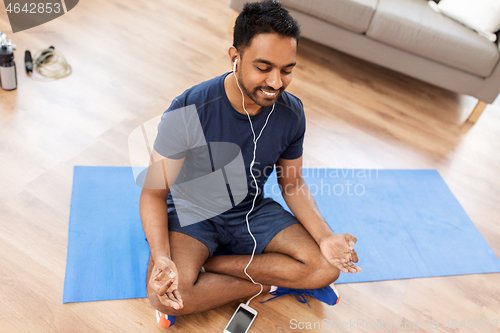 Image of indian man meditating in lotus pose at home