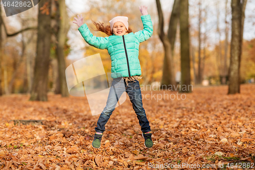 Image of happy girl jumping and having fun at autumn park