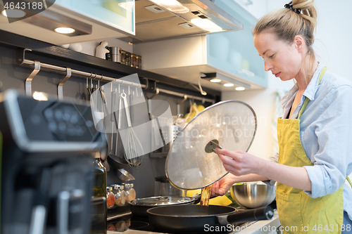 Image of Stay at home housewife woman cooking in kitchen, stir frying dish in a saucepan, preparing food for family dinner.