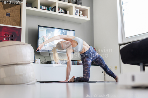 Image of Attractive sporty woman working out at home, doing pilates exercise in front of television in her living room. Social distancing. Stay healthy and stay at home during corona virus pandemic