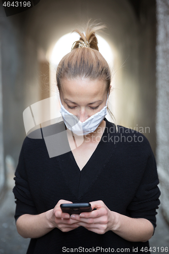 Image of COVID-19 pandemic coronavirus. Casual caucasian woman at medieval city street using mobile phone, wearing protective face mask against spreading of coronavirus and disease transmission