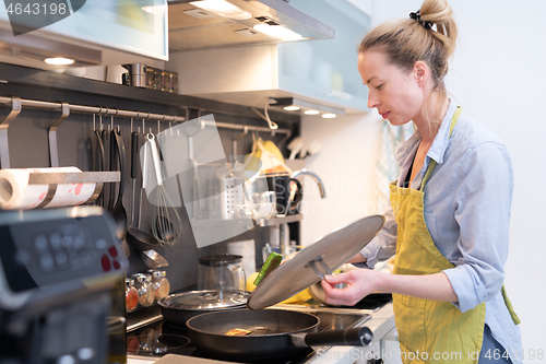 Image of Stay at home housewife woman cooking in kitchen, stir frying dish in a saucepan, preparing food for family dinner.