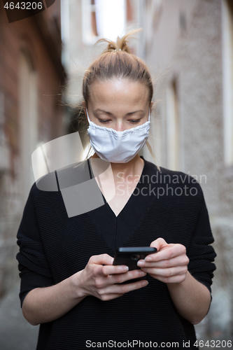 Image of COVID-19 pandemic coronavirus. Casual caucasian woman at medieval city street using mobile phone, wearing protective face mask against spreading of coronavirus and disease transmission