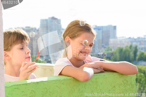 Image of Girl blowing soap bubbles one of which burst at the face of another girl