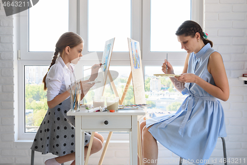 Image of The girl learns to paint at the tutor, together they draw at the window