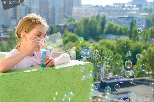 Image of Girl blows hearty soap bubbles from the balcony of a high-rise building