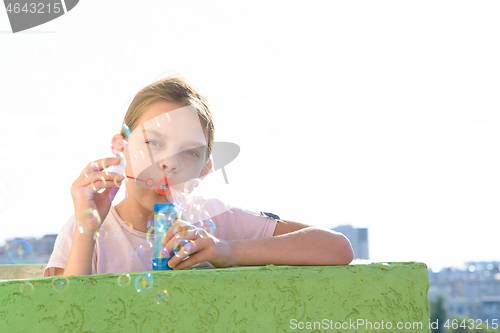 Image of The girl blows bubbles on the balcony of a high-rise building, and looked into the frame