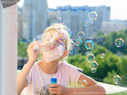 Image of Girl blows a lot of soap bubbles from the balcony of the house