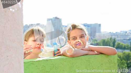 Image of Girl watching her sister blow bubbles on the balcony of the house