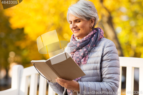 Image of happy senior woman reading diary at autumn park