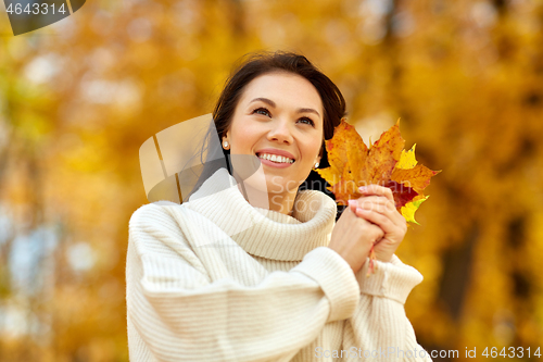 Image of happy young woman with maple leaves in autumn park