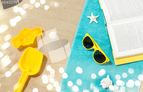 Image of sunglasses, sand toys and book on beach towel