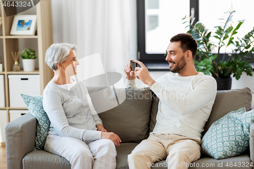 Image of adult son photographing senior mother at home