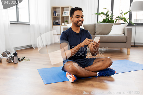 Image of indian man with smartphone on exercise mat at home