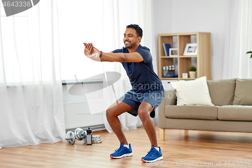 Image of indian man exercising and doing squats at home