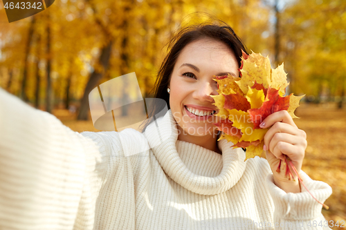 Image of woman with leaves taking selfie in autumn park