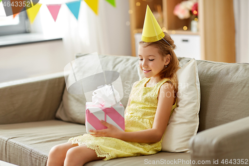 Image of happy girl in party hat with birthday gift at home