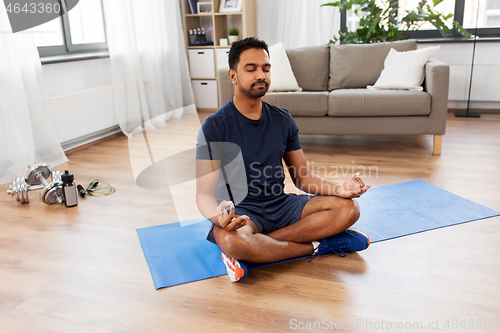 Image of indian man meditating in lotus pose at home