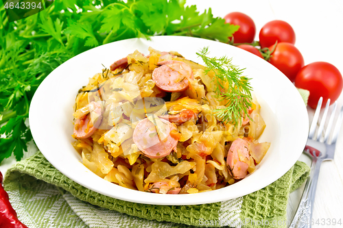 Image of Cabbage stew with sausages in white plate on board