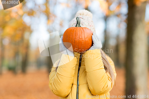 Image of girl hiding her face behind pumpkin at autumn park